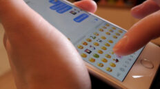 Hands typing emojis on a mobile phone keyboard