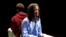 Two young men sit in chairs back to back