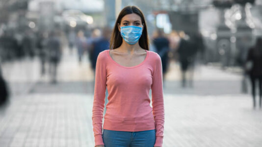 A young girl wearing a COVID mask feeling alone in public.