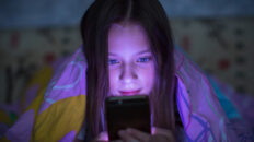 A young girl stares at her phone in bed