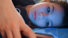 A tired young girl on her phone in bed