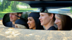 Graduates appear in the rear view mirror of an automobile