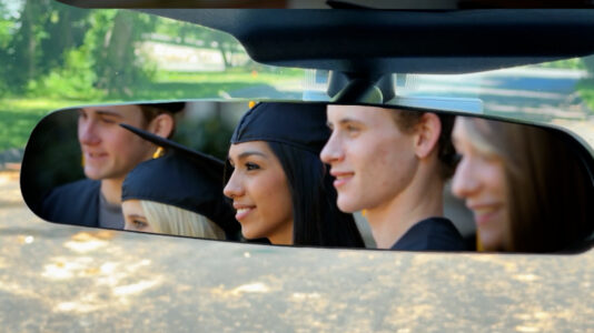 Graduates appear in the rear view mirror of an automobile